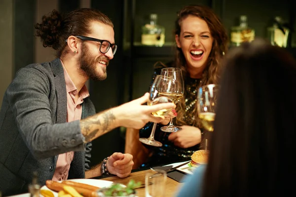 Fröhliche Gruppe von Freunden sitzt im Restaurant zum Abendessen und prostet zu. — Stockfoto