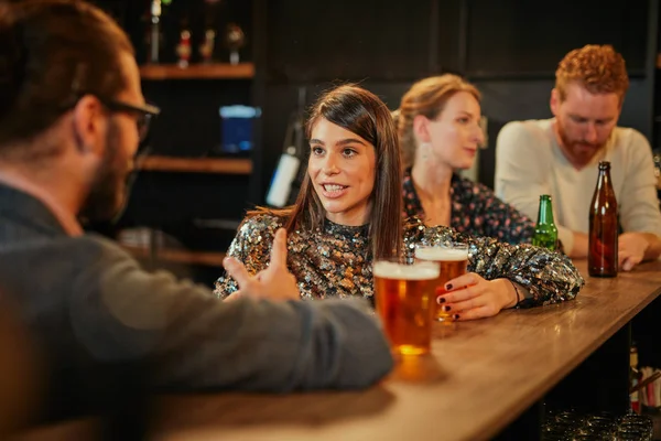 Achteraanzicht van een knappe blanke man leunend op een bar, bier drinkend en flirtend met een vrouw die hij net ontmoette. Pub interieur. — Stockfoto