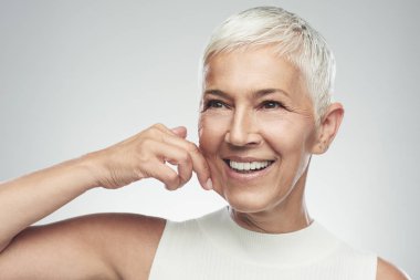 Muhteşem gülümseyen Beyaz yaşlı kadın kısa gri saçları yanağını çimdikleme ile. Güzellik fotoğrafçılığı.