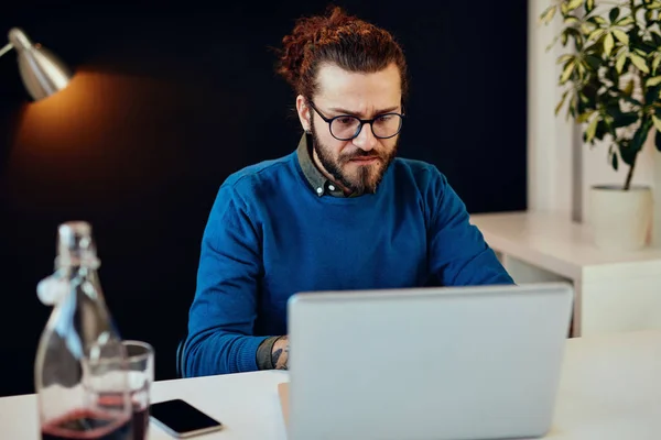 Bonito homem de negócios barbudo caucasiano sentado em seu escritório moderno e usando laptop para escrever relatório. — Fotografia de Stock