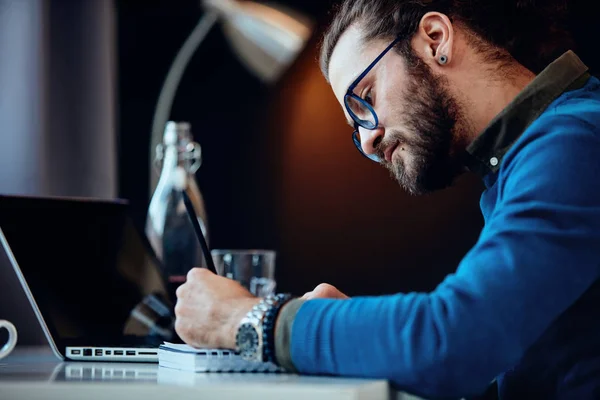 Närbild av dedikerad innovativ kaukasisk affärsman sitter på sitt kontor och skriver affärsplan i anteckningsbok. — Stockfoto