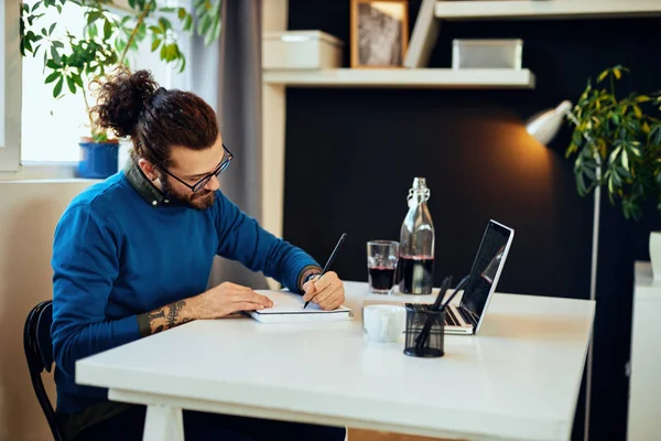 Kreativ kaukasisk skäggig grafisk designer sitter på sitt kontor och ritar i anteckningsbok. — Stockfoto