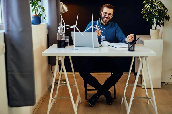 Jonge innovatieve Kaukasische bebaarde ingenieur zit in zijn kantoor en werkt aan duurzame ontwikkeling. — Stockfoto