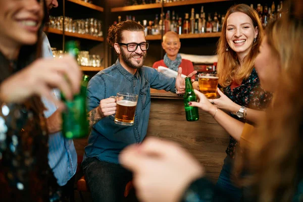 Malá skupinka lidí stojí v hospodě, klábosí, pije pivo a užívá si páteční noci. Noc.. — Stock fotografie