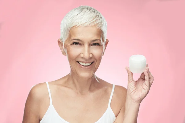 Gorgeous smiling Caucasian senior woman trying out new anti age cream and looking at camera. Beauty photography. — Stock Photo, Image