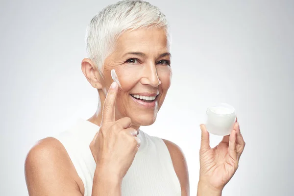 Gorgeous leende kaukasiska Senior Kvinna provar nya anti age Cream. Skönhet fotografi. — Stockfoto