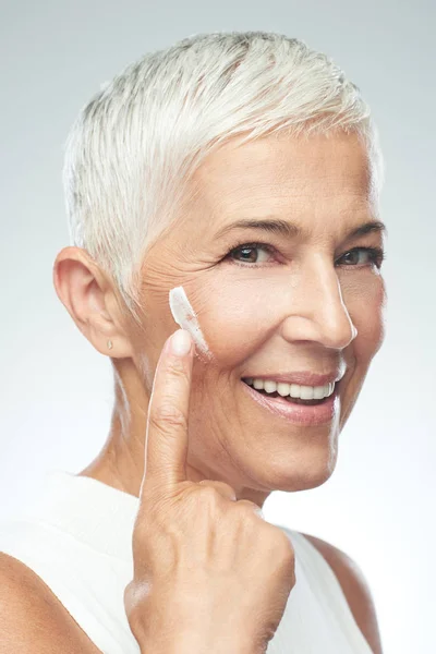 Prachtige glimlachend blanke Senior vrouw uitproberen van nieuwe anti-age crème. Beauty fotografie. — Stockfoto