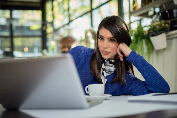 Morena atraente inclinada na mesa e usando laptop enquanto está sentado no café . — Fotografia de Stock