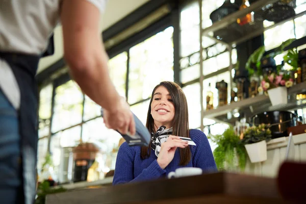 Kaukasische lächelnde Frau bezahlt Rechnung mit Kreditkarte, während sie im Café sitzt. — Stockfoto
