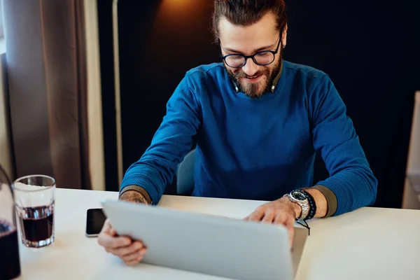 Guapo caucásico barbudo hombre de negocios sentado en su oficina moderna y el uso de ordenador portátil para escribir informe. — Foto de Stock