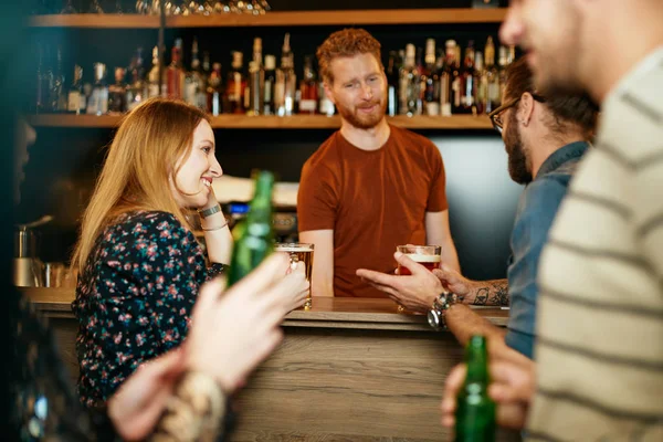 Um pequeno grupo de melhores amigos de pé em um pub, bebendo cerveja, conversando e se divertindo. Concentra-te no barman a limpar copos. Vida noturna . — Fotografia de Stock
