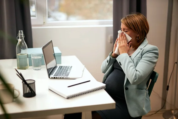 Enferma caucásica embarazada mujer de negocios sentada en su oficina y sonándose la nariz . — Foto de Stock