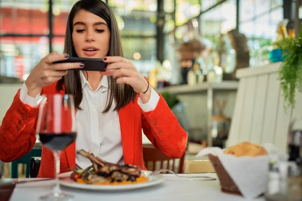 Aantrekkelijke zakenvrouw in pak zitten in restaurant en het nemen van foto van voedsel via de smartphone. — Stockfoto