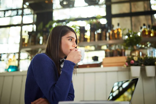 Aantrekkelijke Kaukasische brunette in blauwe trui zittend in café en genietend van verse koffie. Op tafel ligt een laptop. — Stockfoto