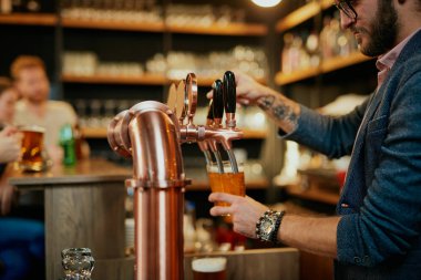 Kafkasyalı dövmeli barmen barda dikilirken bira dolduruyor. Eldeki seçici odaklanma.