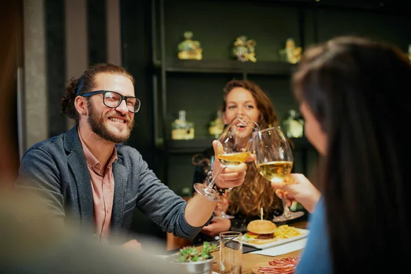 Melhores amigos sentados no restaurante para jantar e fazer um brinde com vinho branco. Na mesa há comida. . — Fotografia de Stock