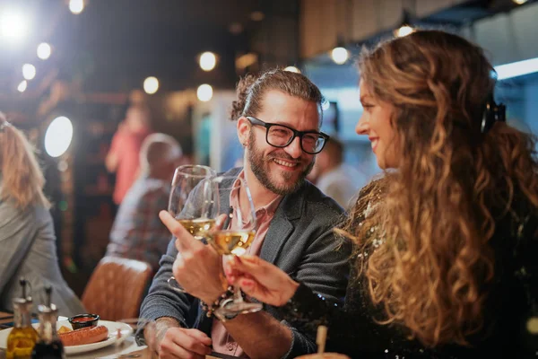 Bonito casal caucasiano sentado no restaurante e aplaudindo com vinho. No fundo são seus amigos . — Fotografia de Stock