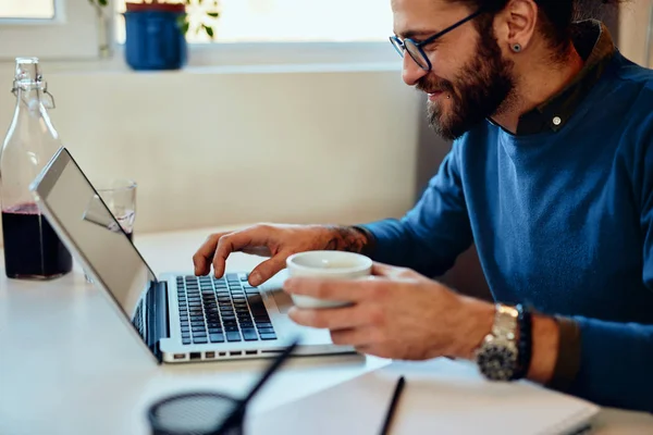 Charmante pigiste caucasien assis dans son bureau à la maison, tapant sur le rapport de l'ordinateur portable et tenant une tasse de café . — Photo