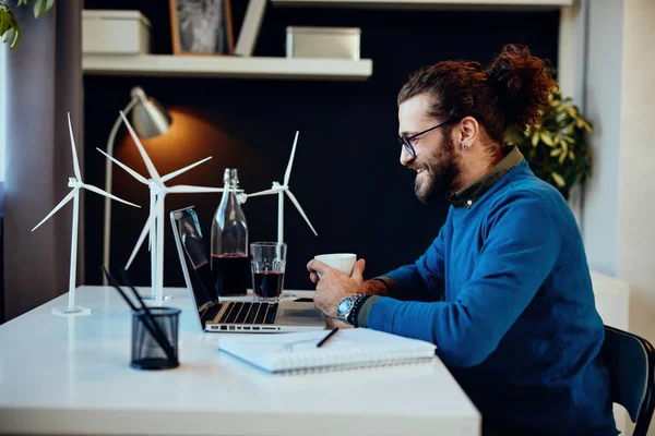 Sjarmerende frilanser som sitter på hjemmekontoret og skriver på PC-rapporten og holder en kopp kaffe. . – stockfoto