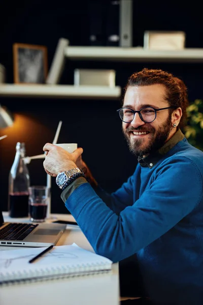 Atractivo empresario barbudo sentado en su oficina, relajarse y beber café . — Foto de Stock