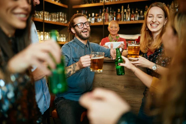 Eine kleine Gruppe bester Freunde steht in einer Kneipe, trinkt Bier, plaudert und amüsiert sich. konzentrieren sich auf Barkeeper, der Trinkglas wischt. Nachtleben. — Stockfoto