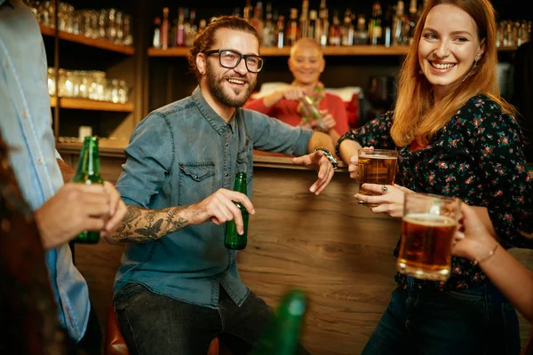 Un pequeño grupo de mejores amigos de pie en un pub, beber cerveza, charlar y divertirse. Concéntrate en el camarero limpiando vasos. Vida nocturna . — Foto de Stock