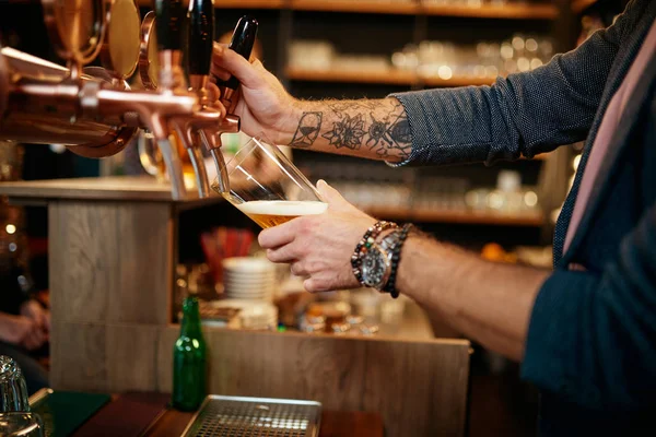 Tätowierter kaukasischer Barmann schenkt Bier aus, während er in der Kneipe steht. — Stockfoto