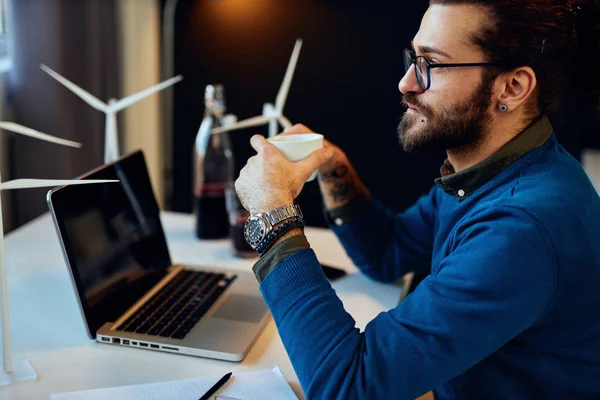 Zijaanzicht van aantrekkelijke bebaarde ondernemer zittend in zijn kantoor, ontspannen en koffie drinken. — Stockfoto