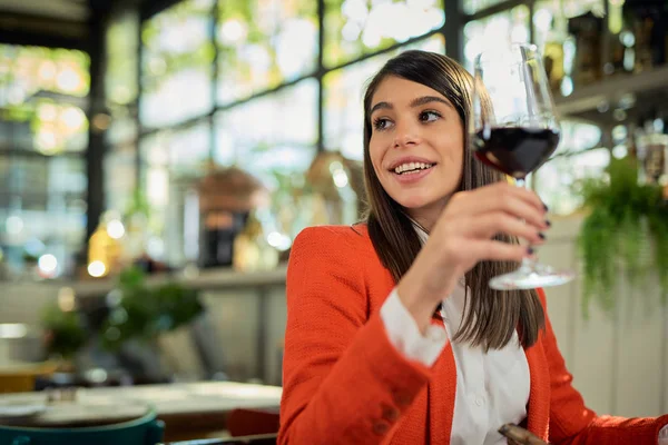 Mosolygó kaukázusi elegáns üzletasszony ül az étteremben, kezében pohár bort, és élvezi az ebédet. — Stock Fotó