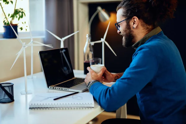 Zijaanzicht van aantrekkelijke bebaarde ondernemer zittend in zijn kantoor, ontspannen en koffie drinken. — Stockfoto