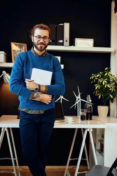 Knappe positieve jonge Kaukasische hipster in zijn kantoor, die papierwerk vasthoudt en zich voorbereidt op een ontmoeting met belangrijke klanten in zijn kantoor. — Stockfoto