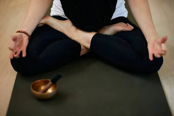 Close up of slim caucasian yogi woman sitting on the mat at home in lotus position and meditating. In front of her is Full Moon Singing Bowl. — ストック写真