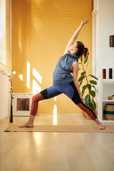 Full length of slim dedicated focused caucasian yogi woman standing in Exalted Crescent Lunge position. Home interior. Morning time. — Stok fotoğraf