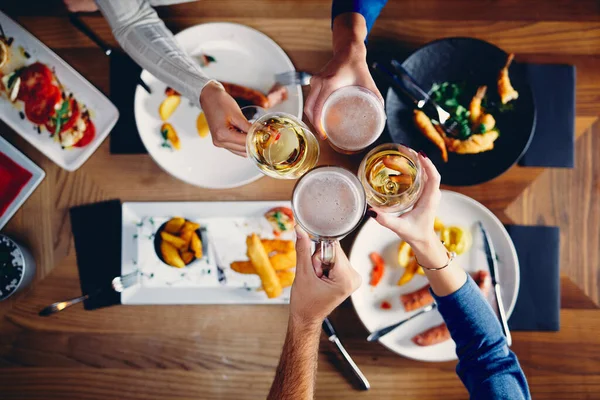 Top view of group of friends sitting ar dinning table, having lunch and toasting with beer. — 스톡 사진