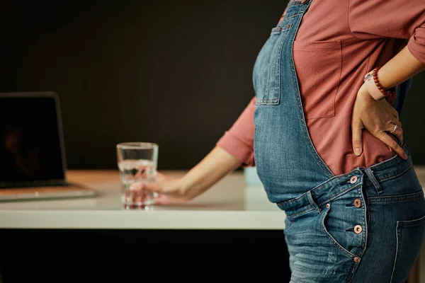 Close-up van zwangere vrouw staan met de hand op taille en leunen op bureau in huis kantoor. — Stockfoto