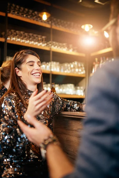 Bella donna caucasica sorridente elegante che tiene la birra e chatta con gli amici. Sullo sfondo c'è il bancone. Pub interno . — Foto Stock