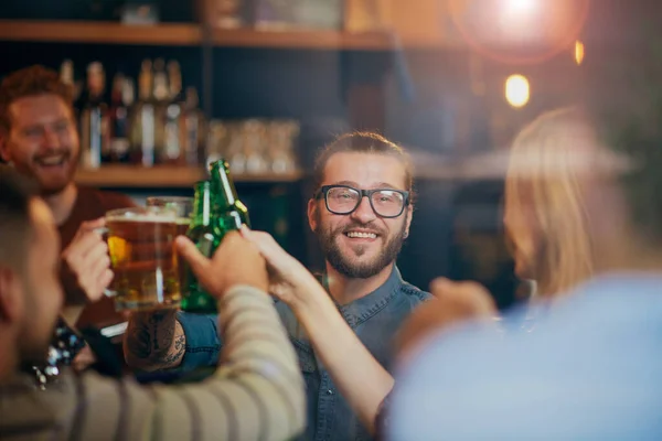 Friends standing in bar and toasting with beer.