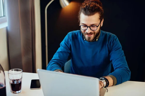 Guapo caucásico barbudo hombre de negocios sentado en su oficina moderna y el uso de ordenador portátil para escribir informe. — Foto de Stock