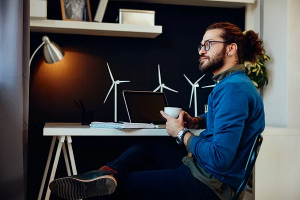 Aantrekkelijke bebaarde ondernemer zit in zijn kantoor, ontspannen en het drinken van koffie. — Stockfoto