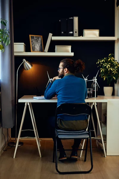 Bakifrån av attraktiv kaukasisk skäggig entreprenör sitter på sitt kontor, tittar genom fönstret och planering strategi för arbete. — Stockfoto