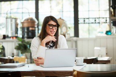 Kafeteryada poz veren çekici beyaz, zarif bir esmer. Masada dizüstü bilgisayar var.