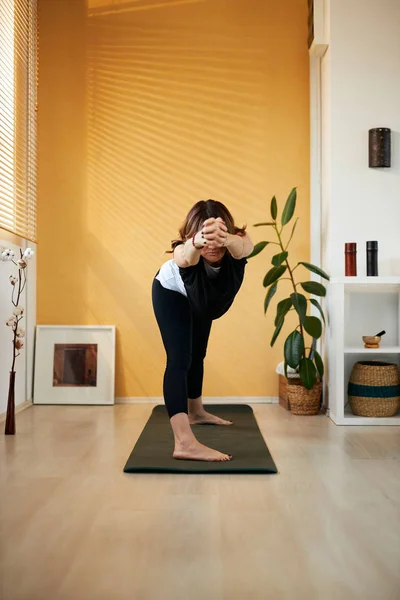 Kaukasische Brünette mittleren Alters steht morgens zu Hause auf einer Yogamatte und praktiziert Yoga. — Stockfoto