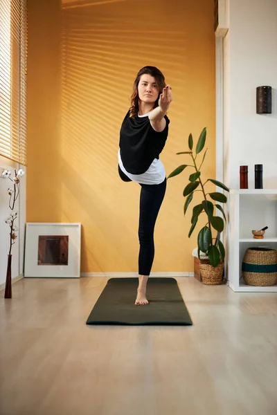 Longitud completa de mujer yogui caucásica delgada de pie sobre un pie en la posición de Señor de la Danza y el equilibrio. Interior del hogar, hora de la mañana . — Foto de Stock