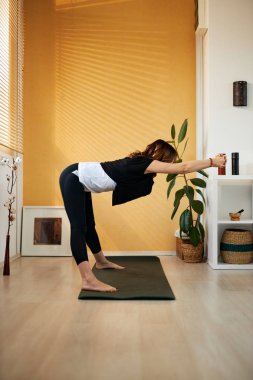 Orta yaşlı beyaz tenli esmer, yoga minderinin üzerinde duruyor ve sabahları evde esniyor..