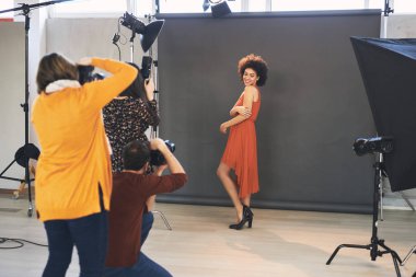 Üç katılımcı stüdyoda duruyor ve güzel bir melez kadın modelin fotoğraflarını çekiyor..