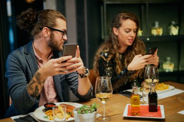 Restoranda oturup akıllı telefonlar kullanan sıkıcı bir çift..