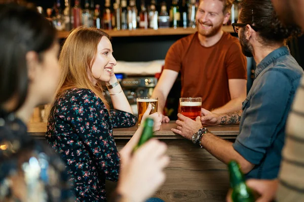 快乐的朋友靠在吧台前 喝啤酒 和酒保聊天 晚上出去 — 图库照片
