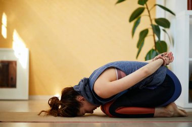 Beyaz tenli, orta yaşlı esmer, çekici bir kadın sabahları Genişletilmiş Çocuk yoga pozu veriyor. İç mimari.