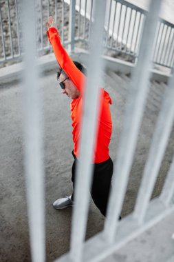 Genç koşucu köprüde dururken koşmak için ısınıyor ve esniyor. Şehir hayatı.