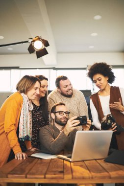 Fotoğrafçılık sınıfından çok kültürlü katılımcılar stüdyoda durup fotoğrafçılık hakkında konuşuyorlar. Eğitmen oturuyor ve onlara kamera parçalarını gösteriyor.